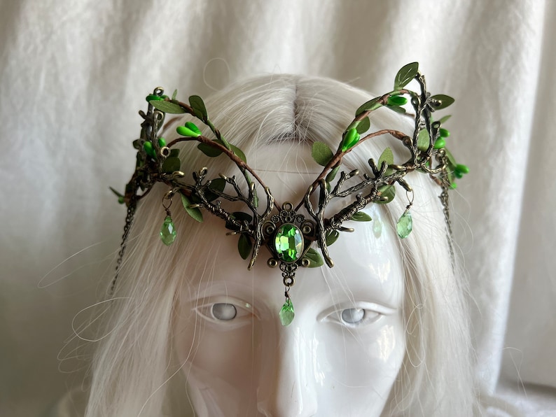 May include: A green and gold leaf crown with green gem accents. The crown is made of metal and has a delicate, intricate design.