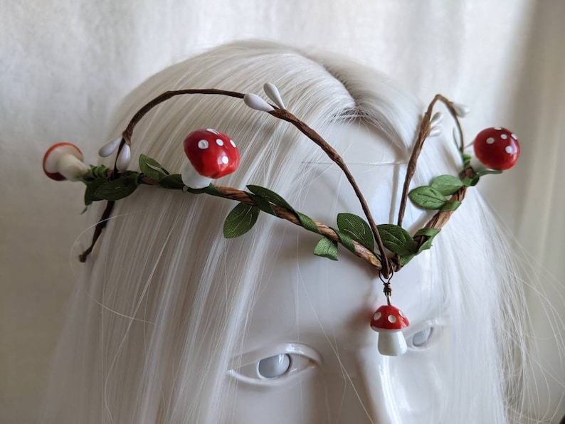 May include: A whimsical forest-themed headband with brown twigs, green leaves, and red and white mushroom accents.