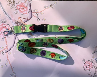 May include: A green lanyard with a colorful cartoon cell print. The lanyard has a black plastic clip and a silver metal hook.