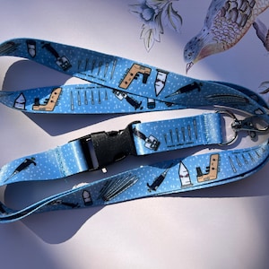 May include: A light blue lanyard with a white background and a repeating pattern of medical tools. The lanyard has a black plastic clip and a silver metal hook.