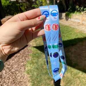 May include: A blue lanyard with a white background and colorful illustrations of science-related items, including petri dishes, test tubes, and a beaker. The text "Agar Plates" is visible on the lanyard.