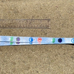 May include: A blue lanyard with a black clip and a silver swivel hook. The lanyard has a repeating pattern of colorful circles and stars.