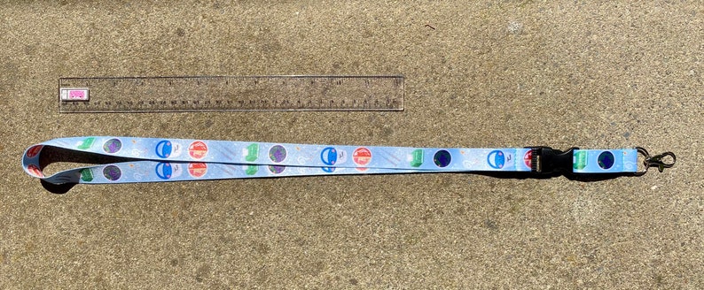 May include: A blue lanyard with a black clip and a silver swivel hook. The lanyard has a repeating pattern of colorful circles and stars.