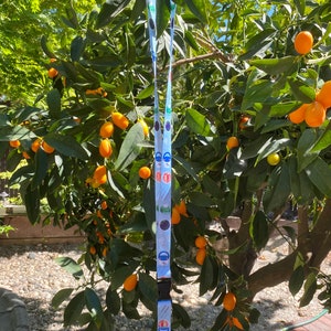 May include: A blue and white lanyard with a variety of colorful designs. The lanyard has a black clip and a silver swivel hook.