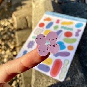 Peut inclure: Une feuille d'autocollants avec différentes formes et motifs. Les autocollants sont de différentes couleurs, notamment le violet, le bleu, le jaune et le rouge. Un autocollant est une fleur violette avec un visage souriant.