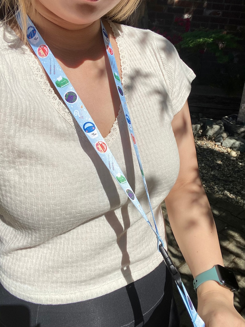 May include: A white shirt with a blue and white lanyard with various colorful icons. The lanyard has a black clip at the bottom.