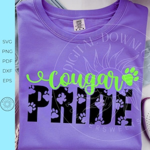 Peut inclure: T-shirt lilas avec l'inscription "Cougar Pride". Le mot "Cougar" est &eacute;crit en vert vif, et "Pride" en noir gras avec des empreintes de pattes. Le t-shirt a un col rond.