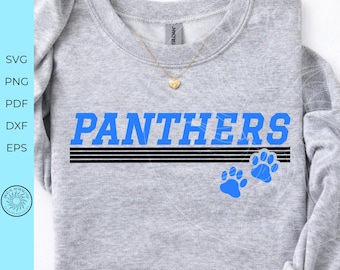 May include: A light gray crewneck sweatshirt featuring the word PANTHERS in bold blue capital letters. Below the text are four horizontal black lines and two blue paw prints. A gold heart-shaped pendant necklace rests on the neckline.