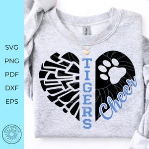 May include: A light gray crewneck sweatshirt featuring a black heart graphic split into two halves. The left side shows a black pom-pom design, while the right side displays a black paw print. The word TIGERS is printed vertically in light blue.