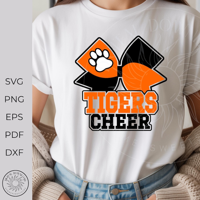Pode incluir: Camiseta branca com um la&ccedil;o laranja e preto com uma pegada branca. A frase "TIGERS CHEER" est&aacute; impressa em laranja e preto. A camiseta &eacute; usada por uma pessoa.