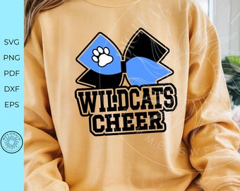 Peut inclure: Sweat-shirt jaune moutarde avec un nœud bleu et noir, une empreinte de patte blanche et l'inscription "WILDCATS CHEER". Le motif est centré sur le devant du sweat-shirt.