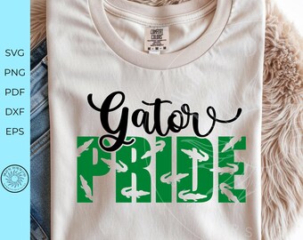 May include: A cream-colored t-shirt featuring the black cursive text Gator above the green block-letter text PRIDE. The green letters contain a repeating white alligator pattern. The shirt has a Comfort Colors brand label at the inner neckline.