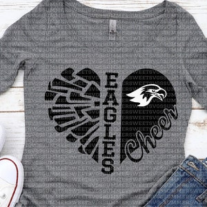 Puede incluir: Una camiseta gris de manga larga con un dise&ntilde;o de coraz&oacute;n negro. El coraz&oacute;n est&aacute; dividido en dos, con el lado izquierdo que presenta un ala de &aacute;guila estilizada y el lado derecho que presenta las palabras "Cheer" y "Eagles".