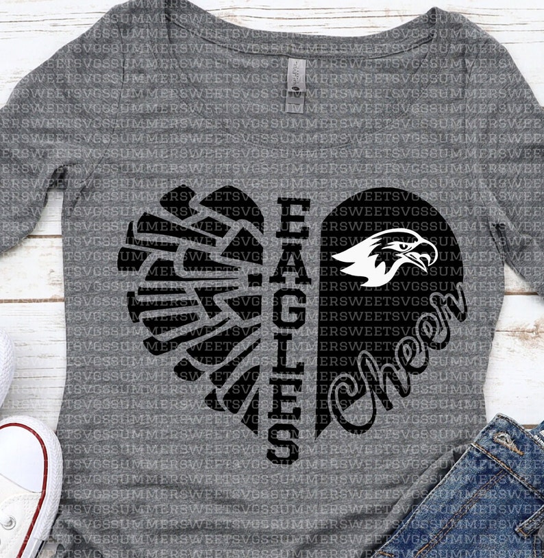 Puede incluir: Una camiseta gris de manga larga con un dise&ntilde;o de coraz&oacute;n negro. El coraz&oacute;n est&aacute; dividido en dos, con el lado izquierdo que presenta un ala de &aacute;guila estilizada y el lado derecho que presenta las palabras "Cheer" y "Eagles".