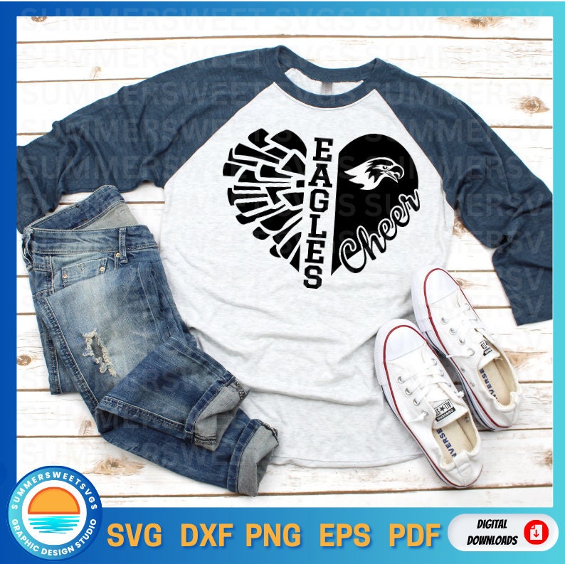 Puede incluir: Una camiseta de b&eacute;isbol blanca y azul con un dise&ntilde;o de coraz&oacute;n negro. El coraz&oacute;n est&aacute; dividido en dos, con el lado izquierdo que presenta un ala de &aacute;guila estilizada y el lado derecho que presenta la palabra "Cheer". El texto "Eagles" est&aacute; escrito verticalmente en el lado izquierdo del coraz&oacute;n.