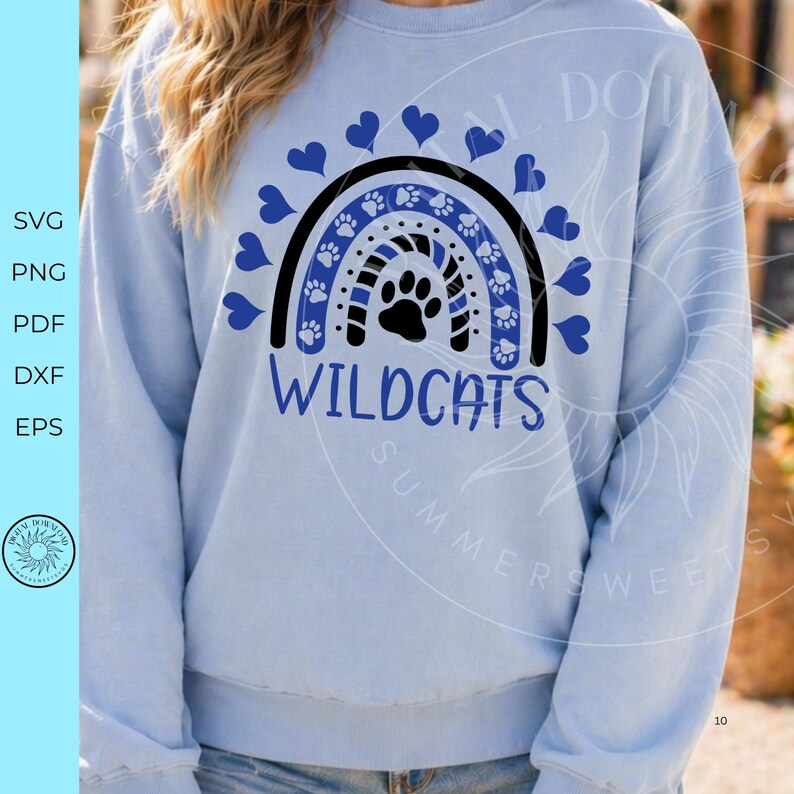 Op de afbeelding: Een lichtblauw sweatshirt met ronde hals en een afbeelding van een regenboog bestaande uit blauwe pootafdrukken en zwarte strepen. Een zwarte pootafdruk staat in het midden van de regenboog, omringd door blauwe hartjes. De tekst WILDCATS is in het blauw gedrukt.