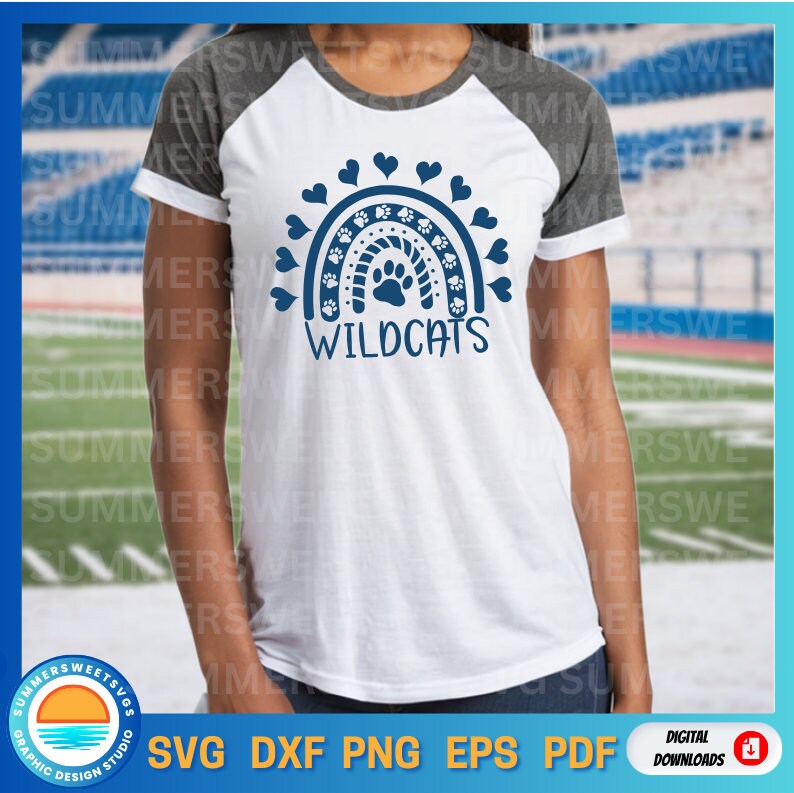 Op de afbeelding: Een wit t-shirt met donkergrijze raglanmouwen met een marineblauwe afbeelding van een regenboog gemaakt van pootafdrukken en hartjes. Het woord WILDCATS staat in marineblauwe hoofdletters onder het regenboogontwerp op de voorkant.