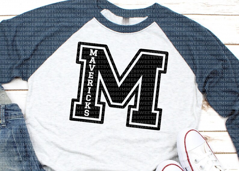 May include: A baseball-style raglan shirt with a light gray heathered torso and dark navy blue sleeves. The front features a large black block letter M with a white outline, and the word MAVERICKS is printed vertically in white inside the letter.