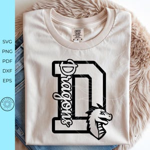 May include: A light beige crew neck t-shirt featuring a large black letter D with the word Dragons written vertically in a script font along the left side of the letter. A black and white dragon head graphic is positioned at the bottom right.