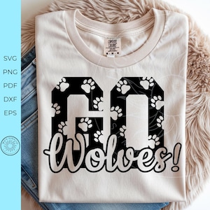 May include: A cream-colored short-sleeve t-shirt featuring a large black graphic with the text GO WOLVES! The letters GO are filled with a white paw print pattern, while the word WOLVES! is written in a white script font below the block letters.