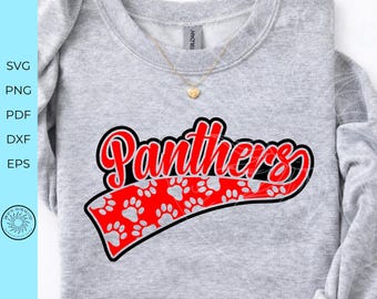 May include: A light gray crewneck sweatshirt featuring the word Panthers in red script with a black outline. Below the text is a red curved banner filled with a repeating pattern of light gray paw prints. A gold heart pendant necklace rests on the collar.
