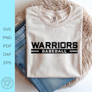May include: A cream-coloured t-shirt displaying the words "WARRIORS BASEBALL" in black, bold lettering. The text is underlined with two black lines. The shirt rests on blue denim jeans and a fluffy, light brown surface.