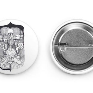 Puede incluir: Un botón blanco y negro con un dibujo de línea detallado de una cara con un tercer ojo y elementos florales.