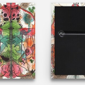 Puede incluir: Un botón colorido con una ilustración de acuarela de un diseño simétrico con una variedad de formas y colores, incluyendo rojo, verde, azul y marrón.