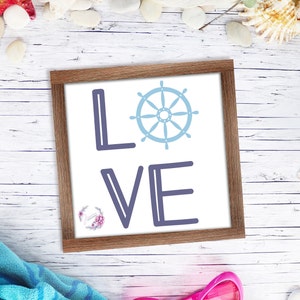 Könnte beinhalten: Ein gerahmtes Schild mit dem Wort "LOVE" in blau-weißen Buchstaben. Das "O" ist durch ein blau-weißes nautisches Rad ersetzt.
