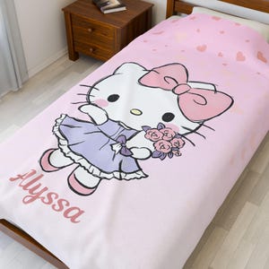 May include: Pink comforter featuring a large illustration of a cartoon cat with a pink bow, holding flowers, and wearing a purple dress. The name "Alyssa" is printed in pink script on the comforter. Small pink hearts are scattered across the top.