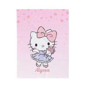 May include: A pink blanket featuring a cartoon illustration of a white cat with a pink bow, wearing a purple dress and holding flowers. The name "Alyssa" is written in pink script at the bottom. The background is light pink with heart shapes.