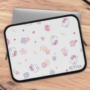 Puede incluir: Funda blanca para portátil con un estampado de caras de Hello Kitty, lazos rosas y flores. El diseño incluye el nombre "ALYSSA". La funda tiene cremallera y ribete negros.