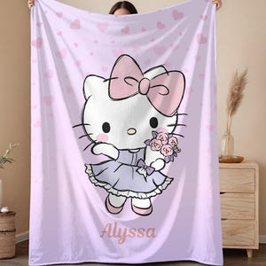 May include: A light purple blanket featuring a cartoon character with a large pink bow, holding flowers. The character is wearing a lavender dress. The blanket has a heart pattern and the name "Alyssa" is printed on it.
