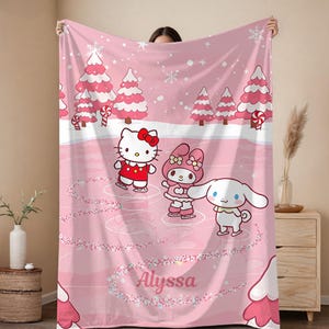 Pode incluir: Cobertor de l&atilde; polar rosa com uma cena de inverno com personagens de desenhos animados patinando no gelo. O cobertor tem um fundo rosa com flocos de neve, &aacute;rvores de Natal e o nome "Alyssa" em it&aacute;lico.