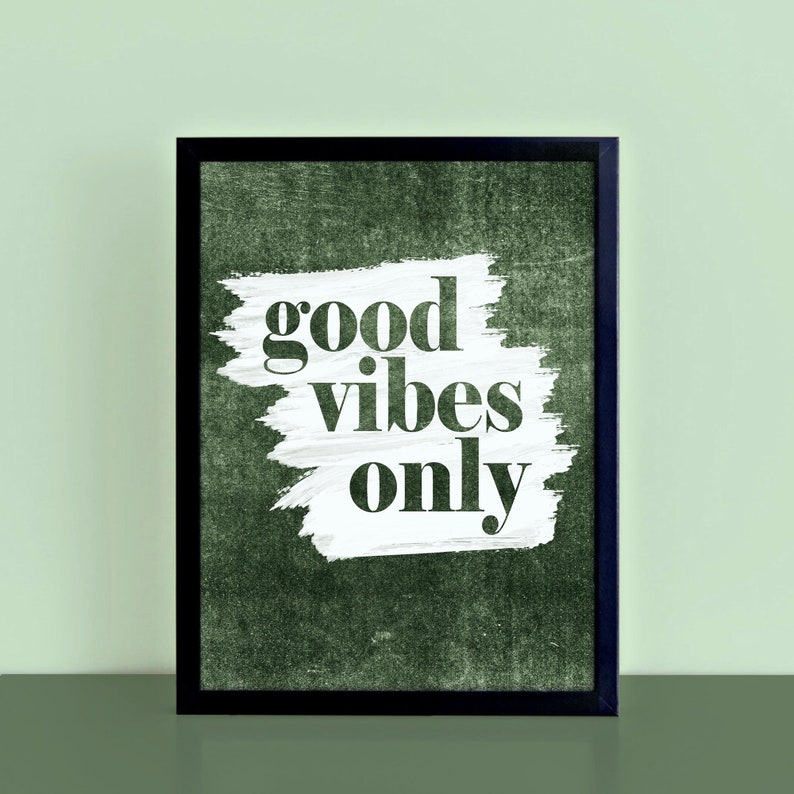May include: A framed art print featuring the phrase "good vibes only" in a bold font. The white text is set against a white brushstroke on a dark green textured background, within a black frame.