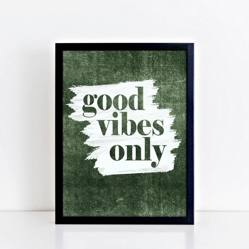 May include: A framed art print featuring the phrase "good vibes only" in a bold, sans-serif font. The text is set against a white brushstroke on a textured, dark green background, within a black frame.