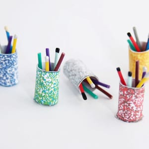 May include: Several pencil holders, each containing pens and pencils of different colours. The holders have a cylindrical shape and are decorated with pixelated patterns in blue, green, yellow, and red. One holder is lying down.