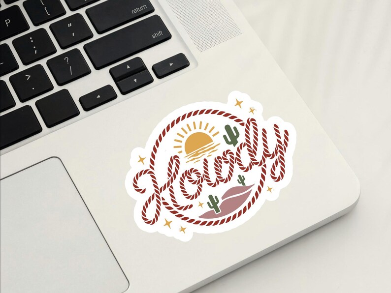 May include: A white sticker with a western-themed design. The sticker features the word "Howdy" in a rope-style font, surrounded by a rope border. The design includes a sun, cacti, and stars.