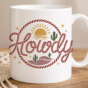 May include: White ceramic mug with a "Howdy" design. The design features a red rope circle with a sunset, cacti, and stars. The word "Howdy" is written in a stylized font with a rope-like texture. A perfect gift for a friend.