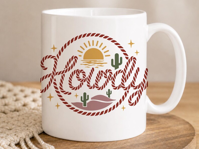 May include: White ceramic mug with a "Howdy" design. The design features a red rope circle with a sunset, cacti, and stars. The word "Howdy" is written in a stylized font with a rope-like texture. A perfect gift for a friend.