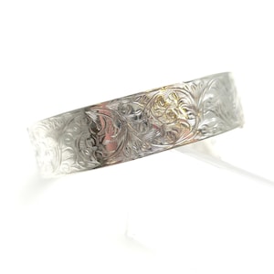 May include: A silver bangle bracelet featuring an engraved floral design. The bracelet has a polished finish and a detailed pattern of leaves and flowers. The design is consistent around the entire bracelet, offering a classic and elegant appearance.