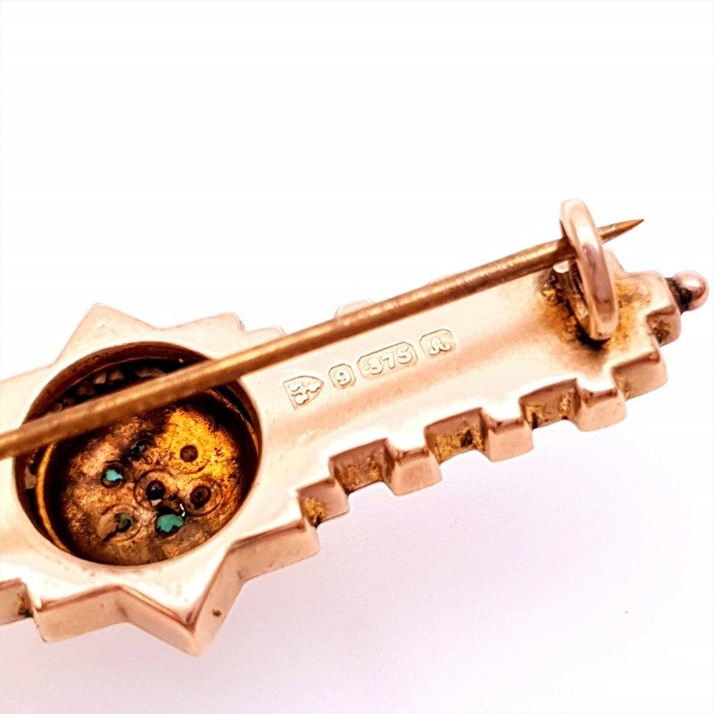 Pu&ograve; includere: Un fermaglio a forma di chiave in oro con un centro a forma di stella e pietre verdi. Il retro del fermaglio ha un marchio che recita "9 375 R".