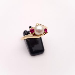 May include: A gold ring with a white pearl and two red ruby stones.