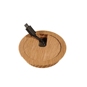 Peut inclure: Un cache-câble rond en bois avec un câble noir qui le traverse. Le cache a une finition en bois naturel lisse.