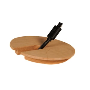 Op de afbeelding: Een houten kabeldoorvoer met een zwarte kabel die er doorheen loopt. De doorvoer is ontworpen om kabels en draden te verbergen.