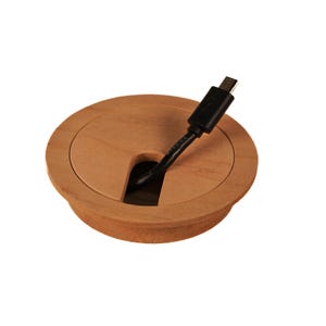 Op de afbeelding: Een ronde, houten kabeldoorvoer met een zwarte kabel die erdoorheen loopt. De afdekking heeft een gladde, lichtbruine afwerking en een licht verhoogde rand.