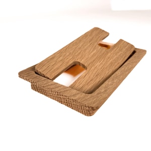 Peut inclure: Un support de téléphone en bois avec un design simple. Le support est composé de deux morceaux de bois empilés l'un sur l'autre. La partie supérieure présente une découpe pour y placer un téléphone.