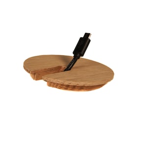 May include: A wooden cable organizer with a split design to hold a cable in place. The organizer is made of light brown wood and has a smooth finish.