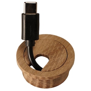 Könnte beinhalten: Eine Holz-Schreibtischdurchführung mit einem schwarzen USB-C-Kabel. Die Durchführung ist kreisförmig mit einer schlüssellochförmigen Öffnung und einer hellbraunen Oberfläche. Das Kabel ist schwarz und hat einen USB-C-Anschluss.