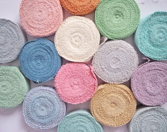 May include: A collection of 12 round fabric rolls in various pastel colors, including light blue, pink, beige, and green. The rolls are arranged in a circle, with the ends of each roll overlapping the next.
